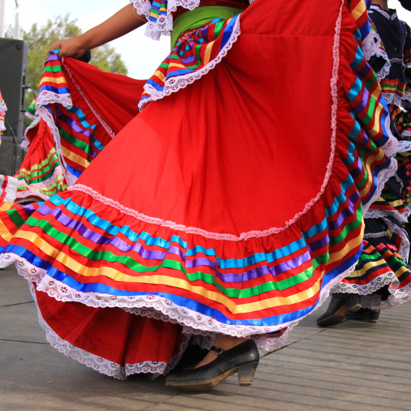 Dancers in bright, multi-colored rainbow-striped skirts swirl during a traditional folk dance on stage.