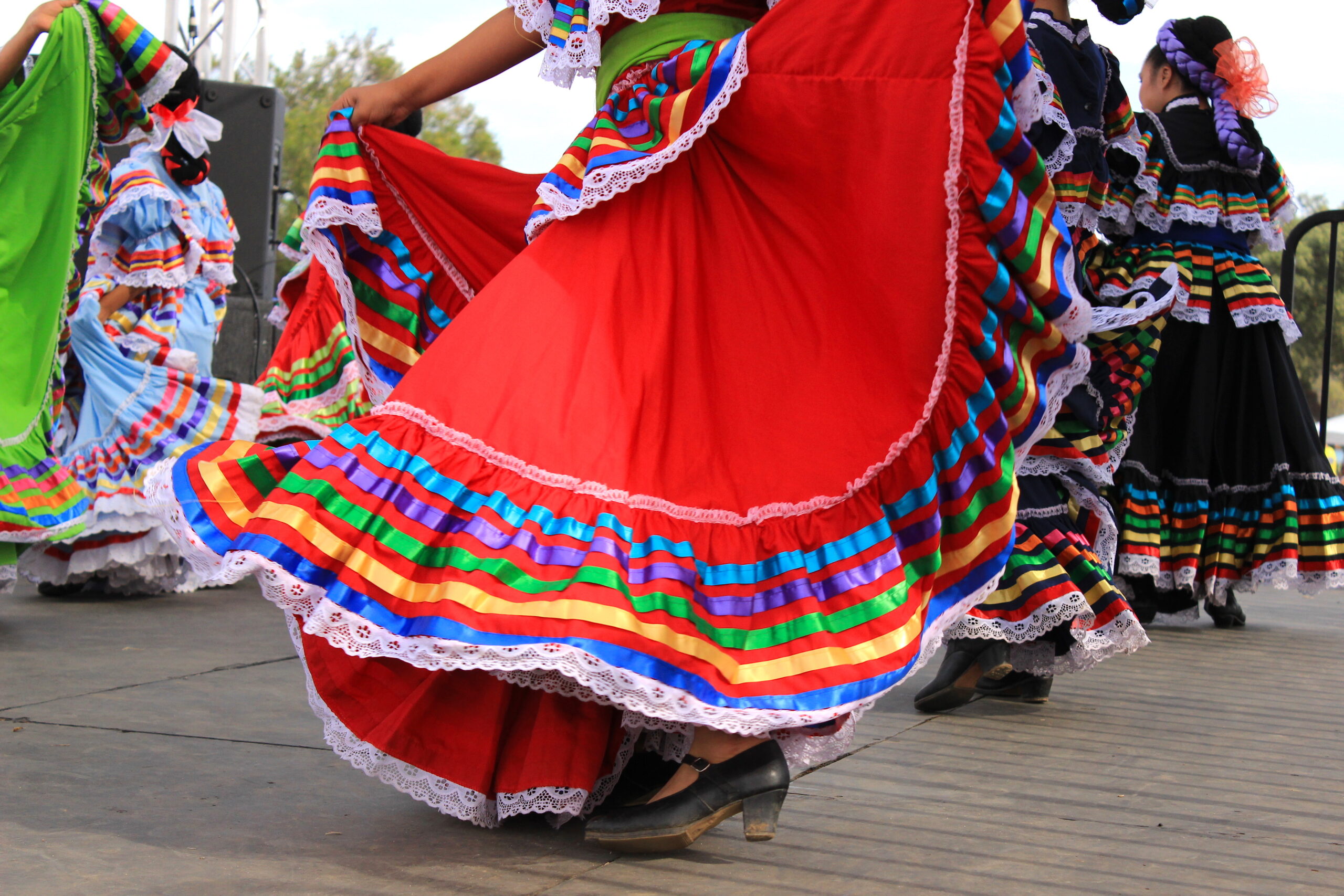 Dancers in bright, multi-colored rainbow-striped skirts swirl during a traditional folk dance on stage.
